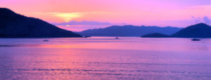 a body of water with mountains surrounding it, with pink, purple, and orange lighting